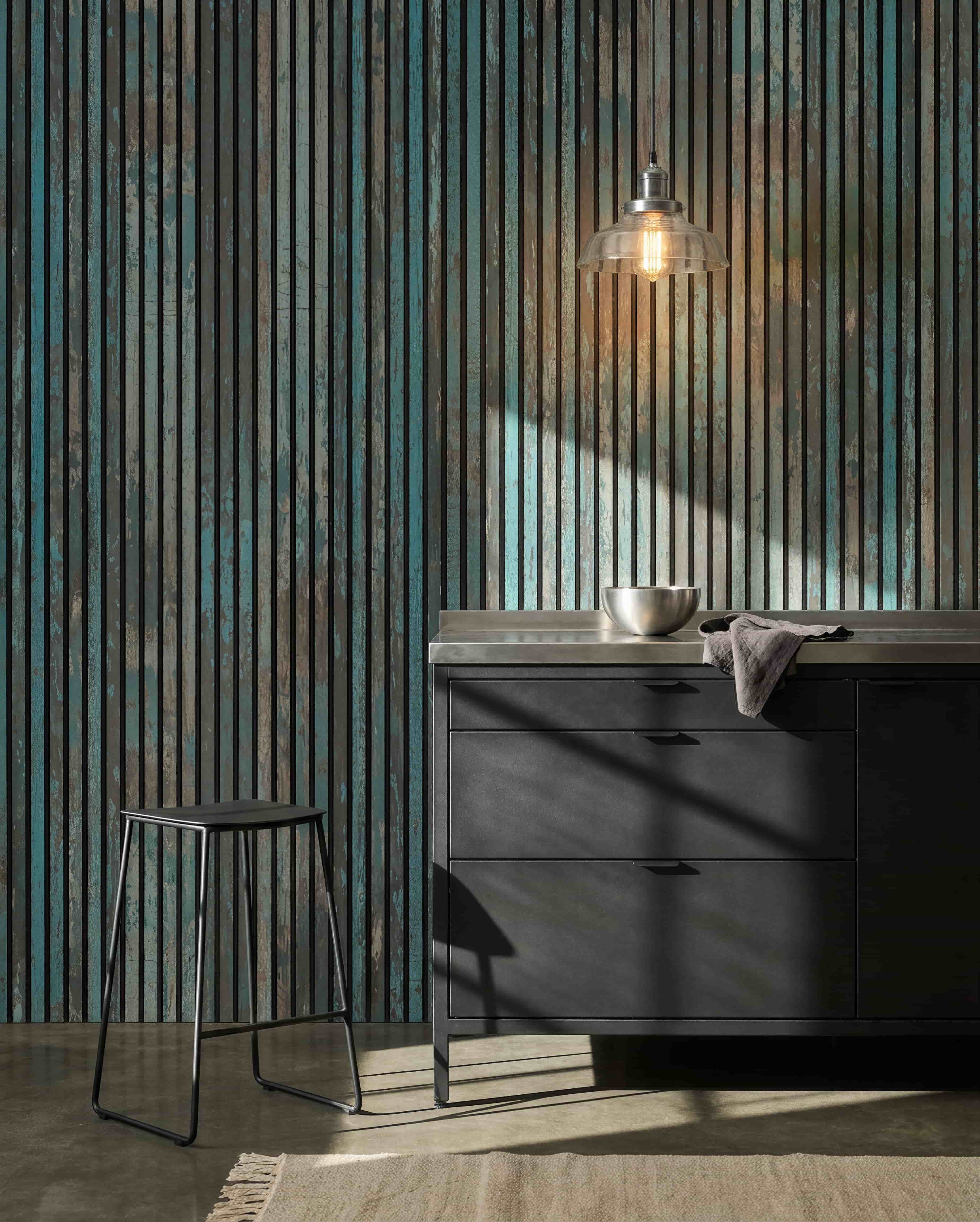 Moderne køkken med sorte taburetter, sorte skabe, en skål under en pære og et WoodUpp Akupanel Oxide Blue akustikpanel på væggen for lydkomfort.